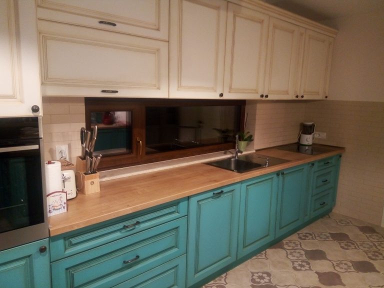 Contrast cromatic între corpurile inferioare din MDF vopsit turcoaz și dulapurile superioare crem într-o bucătărie stil farmhouse.