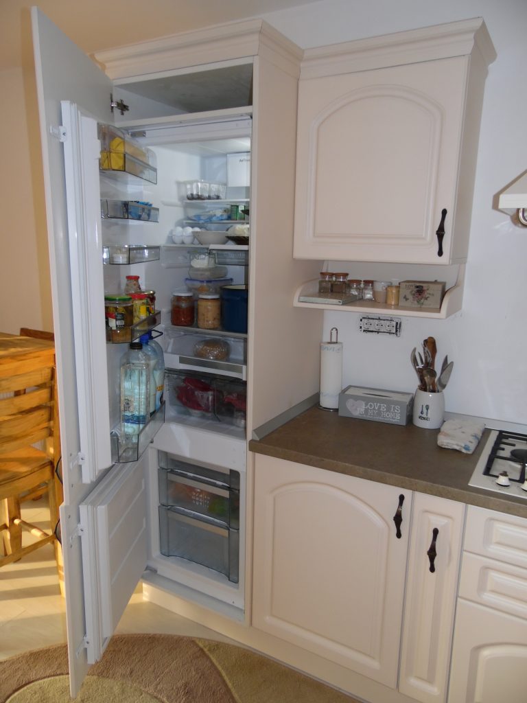 Detaliu cu frigider complet incorporat într-un corp înalt de mobilier de bucătărie clasică din MDF vopsit, cu frezări decorative.