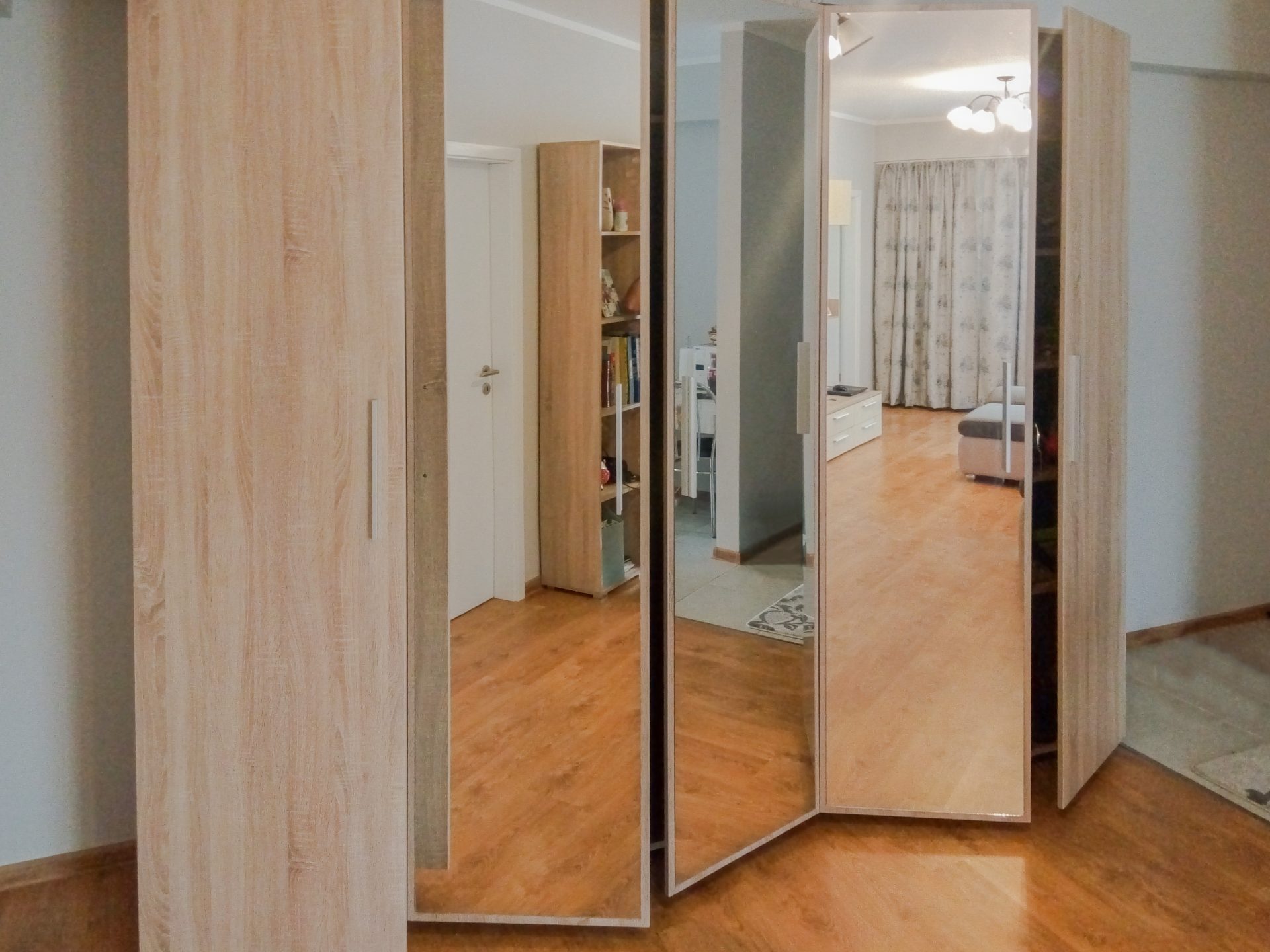 Dressing cu uși batante din PAL stejar și oglindă, parțial deschise, văzut dintr-un unghi lateral.