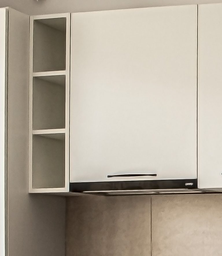 Detaliu cu o etajeră suspendată îngustă, de culoare albă, montată pe perete deasupra blatului, integrată în designul unei bucătării moderne.