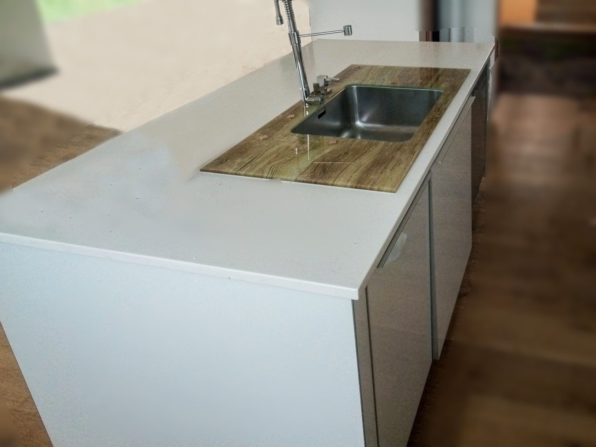 Prim-plan cu o chiuvetă modernă, încastrată într-un blat de sticlă securizată cu finisaj ce imită lemnul, parte dintr-o bucătărie cu blat Corian.