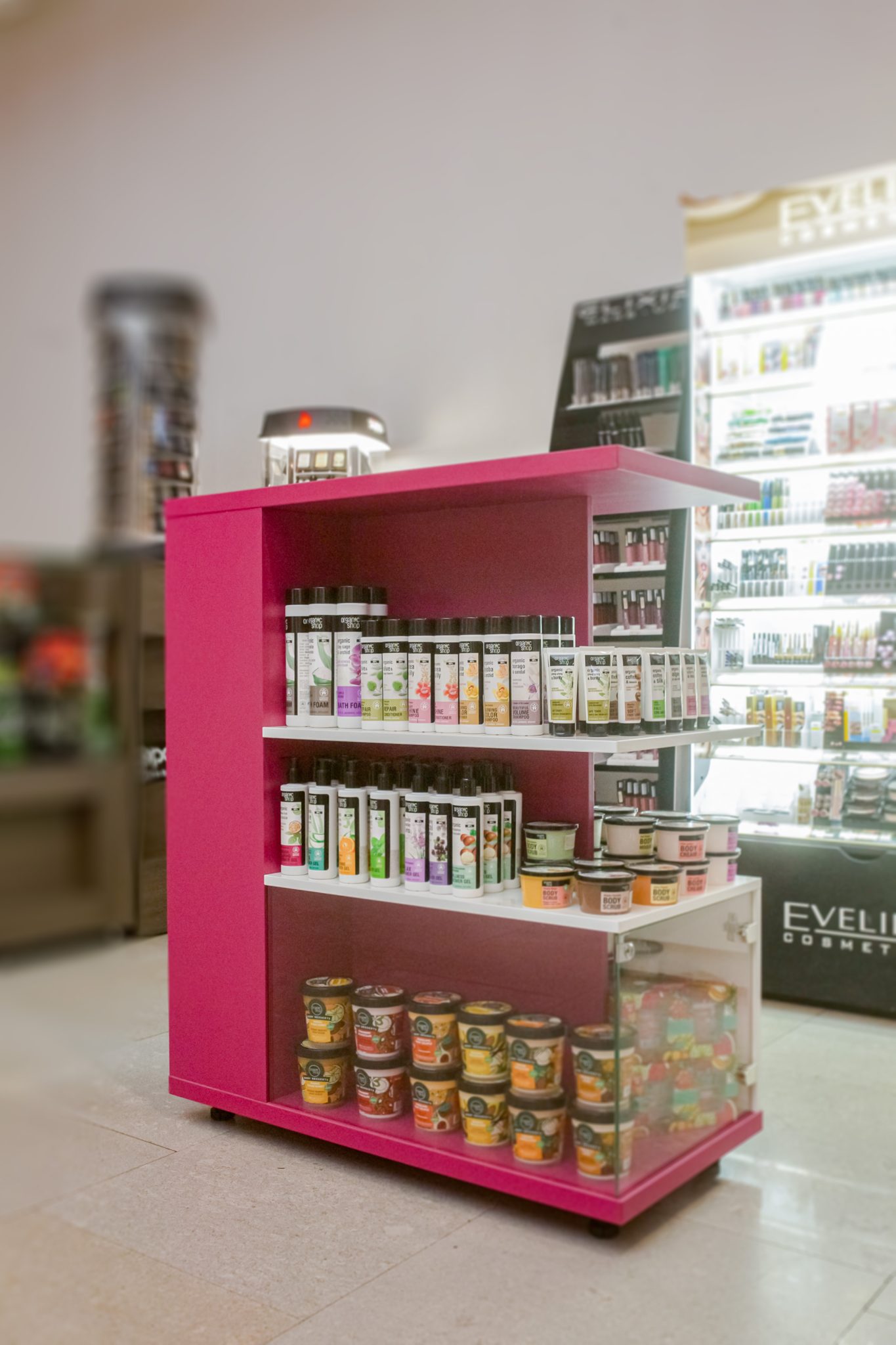 Stand comercial mobil pe roti cu rafturi fixe pentru produse cosmetice.