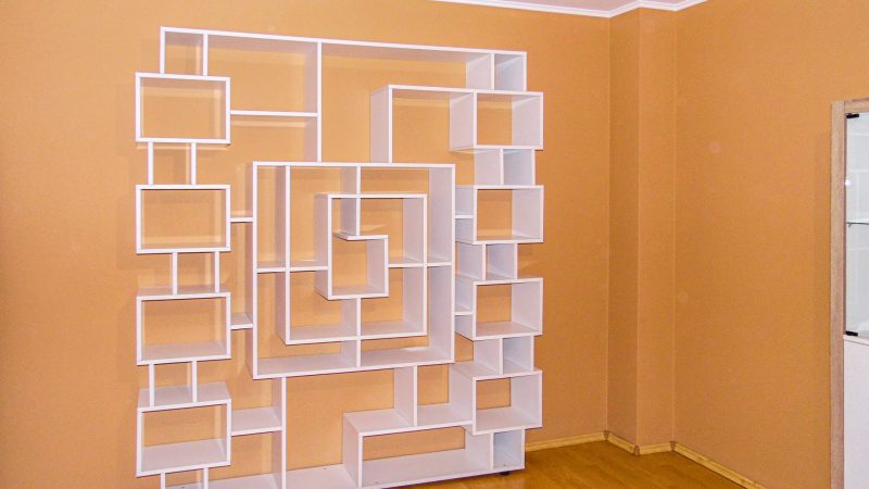 Etajeră albă de perete cu design contemporan, prezentând o compoziție de nișe și cadre asimetrice pentru decor.