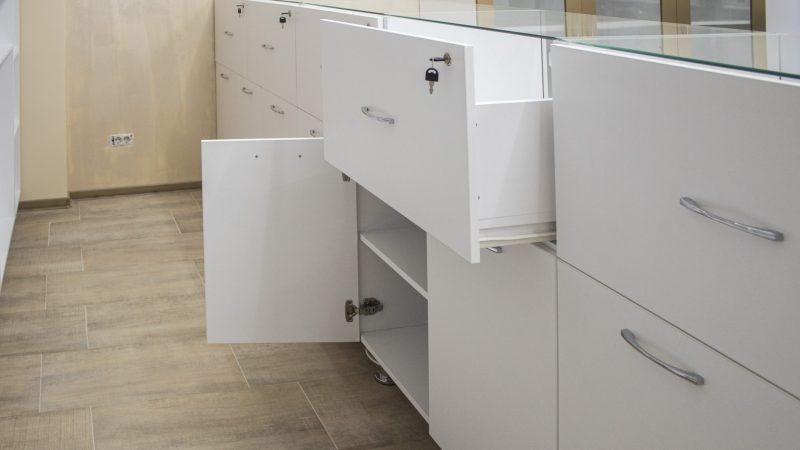 Corpuri joase de depozitare din pal alb mat, cu sertare și uși deschise, pentru spațiu comercial