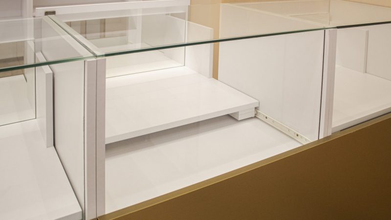 Detaliu close-up cu poliță interioară extractibilă, albă, din interiorul unei vitrine de sticlă