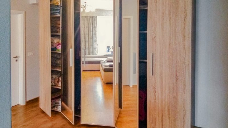 Interiorul unui dressing cu uși batante deschise, arătând organizarea pe rafturi și bare de haine.