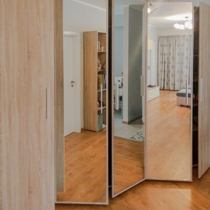 Dressing cu uși batante din PAL stejar și oglindă, parțial deschise, văzut dintr-un unghi lateral.