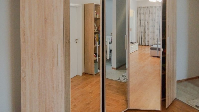 Dressing cu uși batante din PAL stejar și oglindă, parțial deschise, văzut dintr-un unghi lateral.