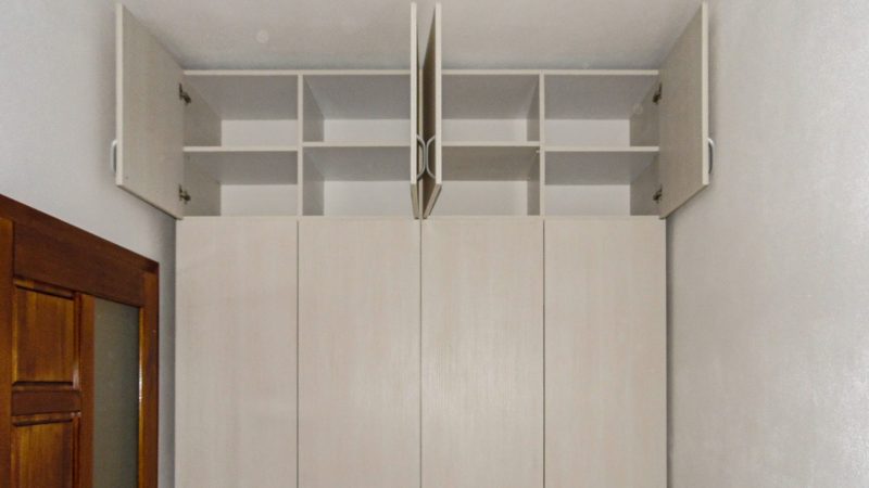 Prin proiectarea dressingului până la tavan, am creat un spațiu de depozitare suplimentar, valoros. Corpurile superioare sunt locul perfect pentru a păstra lucruri de care nu ai nevoie zilnic, eliberând astfel zona de acces principală. Această abordare verticală nu doar că maximizează capacitatea de stocare, dar creează și o prezență vizuală unitară, integrând piesa de mobilier în arhitectura camerei. Rezultatul este un perete întreg dedicat ordinii, unde fiecare lucru își are locul său bine definit.