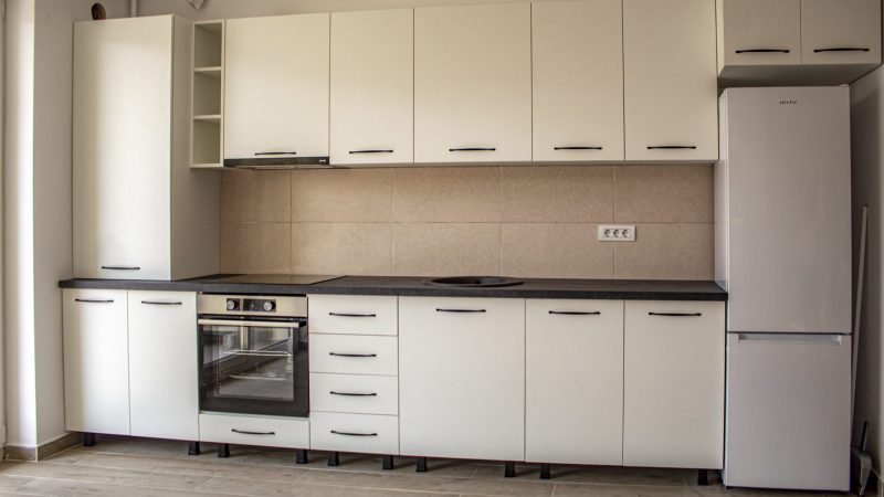 Vedere de ansamblu a unei bucătării moderne realizate din PAL melaminat alb, cu un contrast puternic creat de blatul și accesoriile negre.