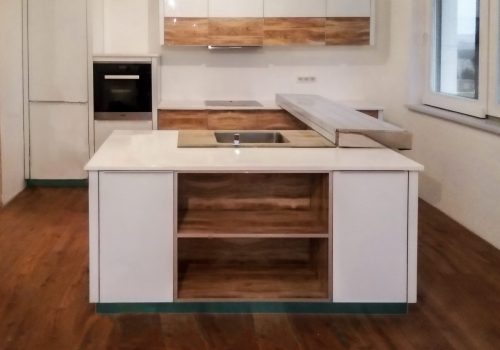 Bucătărie albă modernă cu insulă, văzută din living, cu rafturi decorative din sticlă cu finisaj de lemn care adaugă căldură vizuală.